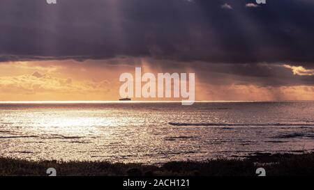 Sturm auf dem Pazifik Küste mit Sonnenstrahlen durch die dunklen Wolken; helles Licht im Hintergrund und Frachtschiff silhouette visib Stockfoto