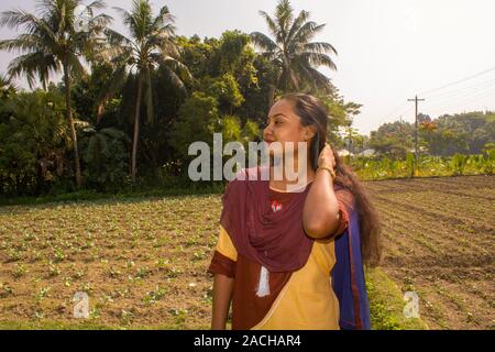 Porträt einer niedlichen, Braun, verspielte Mädchen (Bangladeshi oder Südasiatischen), sie hat lange schöne Haare, leere Feld und Bäume im Hintergrund Stockfoto