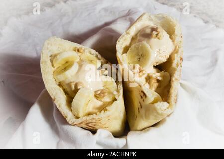 Pita Tasche Brot gefüllt mit Karamell-eis, Walnüsse und Bananenscheiben, bereit zu essen, auf alten weißen Tuch Stockfoto