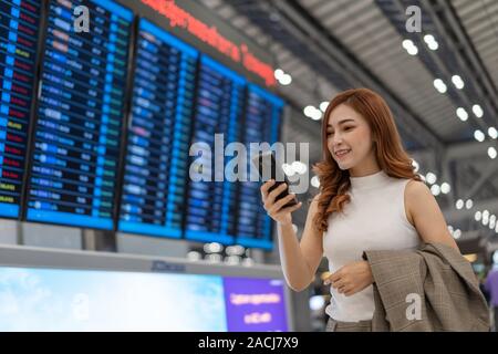 Schöne Frau mit Flug Infotafel am Flughafen smartphone Stockfoto