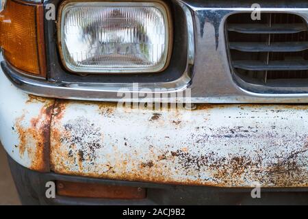 Tatorts bis zu Verfall und Rost auf den vorderen Stoßfänger eines alten weißen Lkw. Rost Loch auf alten, abgenutzten Oberfläche aus lackiertem Metall. Stockfoto