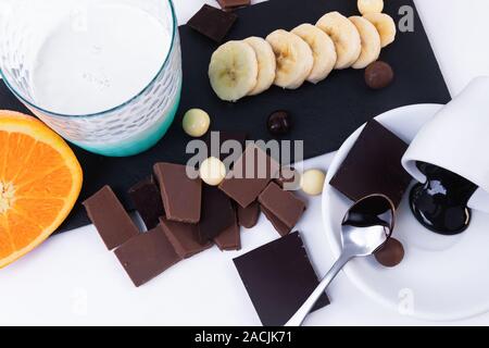 Teile der dunklen Schokolade, Chocolate Chips Banane ein Glas Milch isoliert. Horizontale Komposition. Ansicht von oben Stockfoto