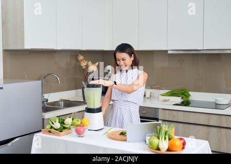 Schöne asiatische Frau entsaften, grüner Saft mit Saft Maschine in der Küche zu Hause. Gesundes Konzept. Stockfoto