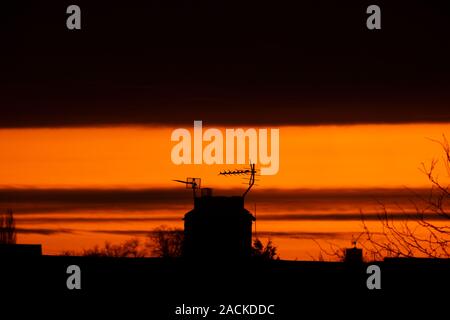 Wimbledon, London, UK. 3. Dezember 2019. Eine dünne Splitter des Fernen orange Sunrise unter einer Decke von Wolke über Suburban Dächer in South West London. Credit: Malcolm Park/Alamy Leben Nachrichten. Stockfoto