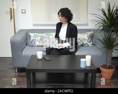 Moderne Unternehmen kaukasische Frau Schreiben auf Ihrem Laptop, auf den Knien, sie sitzt auf dem Sofa. Sie arbeitet aus Ihrem Haus, online arbeiten, Stockfoto