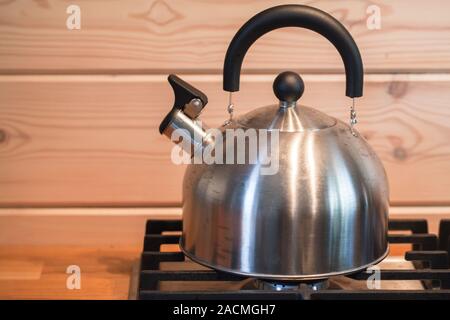 Edelstahl pfeifen Wasserkocher auf einem Gasherd mit Holzwänden auf einem Hintergrund steht Stockfoto