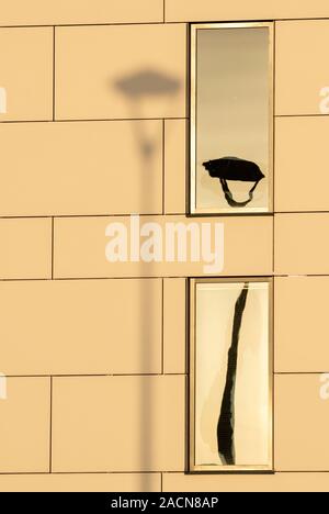 Der Lampenpfahl wirft Schatten an die Wand mit seiner Reflexion in einem Fenster als kreative abstrakte künstlerische Komposition. Stockfoto