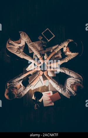 Hohe Winkel über Ansicht vertikale Foto von vier Leuten, die Kollegen sitzen Tabelle arbeiten bis spät in die Nacht Betrieb Stapel Stapel Union ein Team formalwear Stockfoto