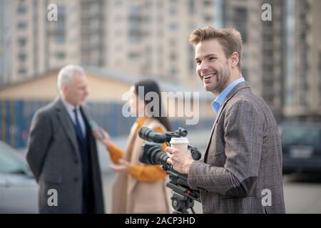 Junge Reporter mit Kaffee in seiner Hand lächelnd Stockfoto