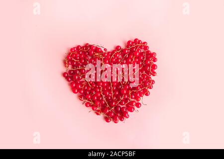 Frische rote Johannisbeeren in der Form eines Herzens auf einem rosa Hintergrund Ernährung und richtige Ernährung Konzept Reif. Stockfoto