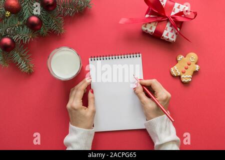 Weihnachten leer Leer schreiben für Santa Claus mit Glas Milch, Kekse, Lebkuchen auf Rot. Frau schreiben Checkliste und Ziele. Platz für Ihren Text. Stockfoto