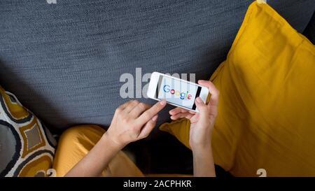 Schließen Sie sich auf Frau Hände halten Smartphone mit Google Logo. Frau mit Handy mit Google Logo auf dem Bildschirm gemütlich zu Hause auf dem Sofa im Wohnzimmer. Stockfoto