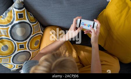 Schließen Sie sich auf Frau Hände halten Smartphone mit Google Logo. Frau mit Handy mit Google Logo auf dem Bildschirm gemütlich zu Hause auf dem Sofa im Wohnzimmer. Stockfoto