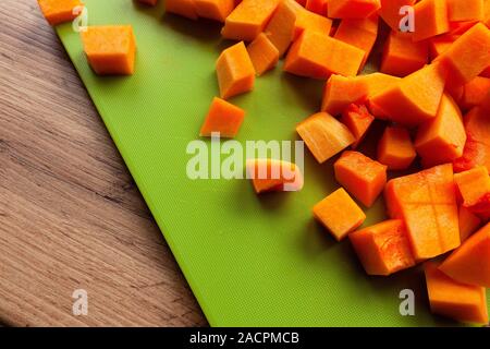 Lebendige und helle orange Kürbis, in Würfel geschnitten auf grün Schneidebrett Stockfoto