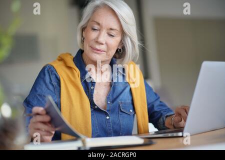 Moderne ältere Frau Kontrolle Tagebuch zu Hause und arbeiten Stockfoto