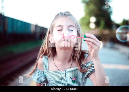 Porträt einer wunderschönen kleinen Mädchen bläst Seifenblasen. Ein Kind spielt mit Blasen, auf grünem Hintergrund. Im Freien Stockfoto