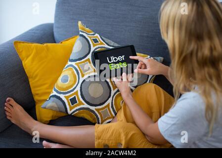 Schließen Sie sich auf Frau Hände halten Smartphone mit UberEats Logo. Junge Frau mit Smartphone mit Uber isst Logo auf dem Bildschirm gemütlich zu Hause auf dem Sofa Stockfoto