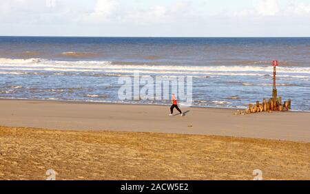 Ein Mann läuft an der Küste am Strand an der Küste von Norfolk in Bacton-on-Sea, Norfolk, England, Vereinigtes Königreich, Europa. Stockfoto