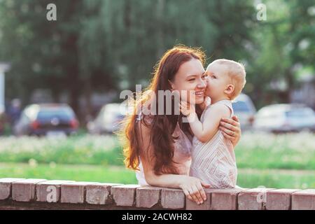 Kleines Mädchen küsst sie Mama beim Spaziergang im Park Stockfoto