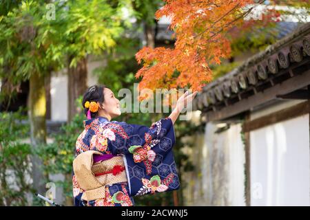 Geishas Mädchen mit japanischen kimono unter roten Holz- Tori Gate bei Fushimi Inari Schrein in Kyoto, Kimono ist ein traditionelles japanisches Gewand. Das Wort " Stockfoto