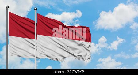 Monaco und Indonesien Flagge im Wind gegen Weiße bewölkt blauer Himmel zusammen. Diplomatie Konzept, internationale Beziehungen. Stockfoto