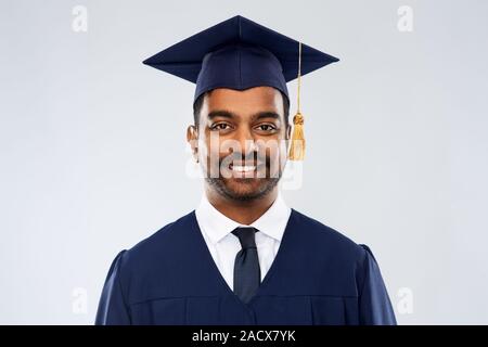 Bildung, Graduierung und Personen Konzept - Glücklich lächelnde indischen männlichen Schulabgänger in Mörtel und Bachelor Kleid über grauer Hintergrund Stockfoto