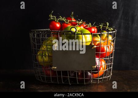 Verschiedene Tomaten in einem Drahtkorb auf einem dunklen Hintergrund Stockfoto