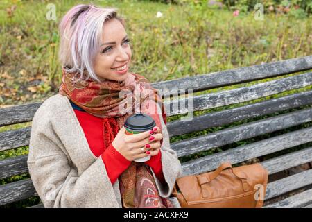 Junge Frau sitzt auf einer Bank und hält eine Tasse Kaffee in der Hand. Stockfoto