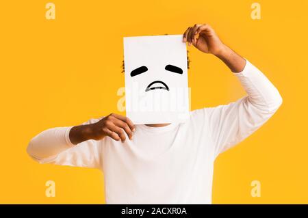 Schwarzer Mann, Papier mit traurigen Emoji über sein Gesicht Stockfoto