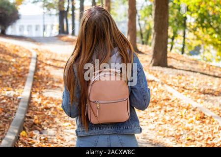 Eine junge Frau mit einem Rucksack Spaziergänge im Park an einem Herbsttag. Reisen rund um die Stadt. Der Blick von der Rückseite. Stockfoto