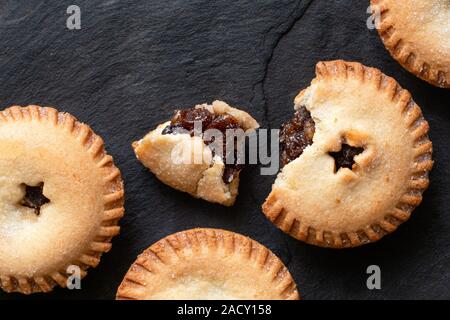 Gebrochen öffnen traditionelle britische Weihnachten Kuchen mit Obst Neben ganze Torten auf schwarzem Schiefer mince Füllung Hackfleisch. Ansicht von oben. Kopieren Sie Platz. Stockfoto