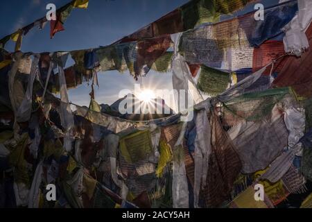 Sonne hinter dem Gipfel des Mt. Everest, vom Gipfel des Gokyo Ri gesehen, durch Tibetische Gebetsfahnen Stockfoto