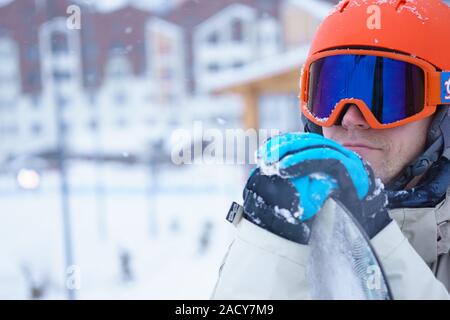 Mann-Snowboarder tragen orange Helm, graue Jacke, schwarze und blaue Handschuhe stehend mit snowboard Stockfoto