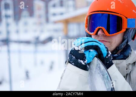 Mann-Snowboarder tragen orange Helm, graue Jacke, schwarze und blaue Handschuhe stehend mit snowboard Stockfoto