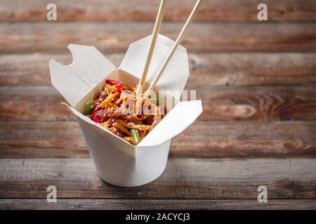 Nudeln mit Schweinefleisch und Gemüse in Take-out Box auf Holztisch Stockfoto