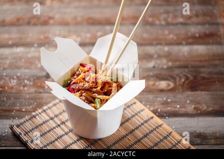 Nudeln mit Schweinefleisch und Gemüse in Take-out Box auf Holztisch Stockfoto