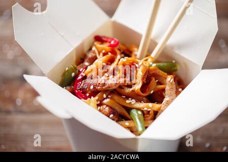 Nudeln mit Schweinefleisch und Gemüse in Take-out Box auf Holztisch Stockfoto