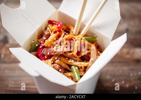 Nudeln mit Schweinefleisch und Gemüse in Take-out Box auf Holztisch Stockfoto