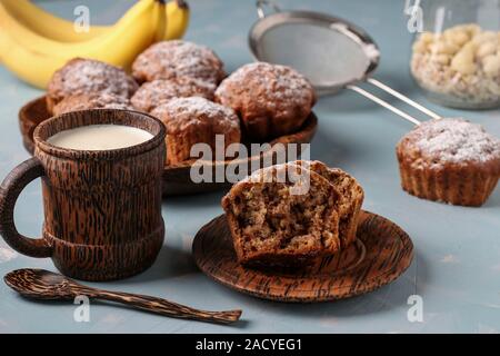 Banana Muffins mit Haferflocken Flocken bestreut mit Puderzucker auf eine Kokosnuss Teller und Tasse Milch, horizontale Ausrichtung Stockfoto