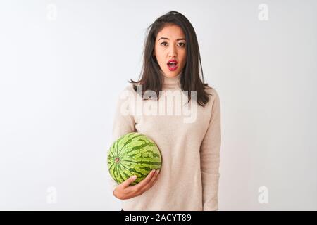 Junge schöne chinesische Frau mit Wassermelone stehend über isoliert weißer Hintergrund Angst im Schlag mit einer Überraschung konfrontiert, ängstlich und aufgeregt mit Stockfoto