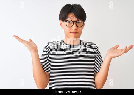 Chinesischer Mann mit Brille und Marine gestreiftes T-Shirt stehend über isoliert weißer Hintergrund ratlos und verwirrt Ausdruck mit Armen und Händen rais Stockfoto