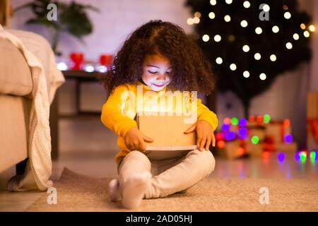 Erstaunt afro Kind öffnen glühende Weihnachtsgeschenk Stockfoto