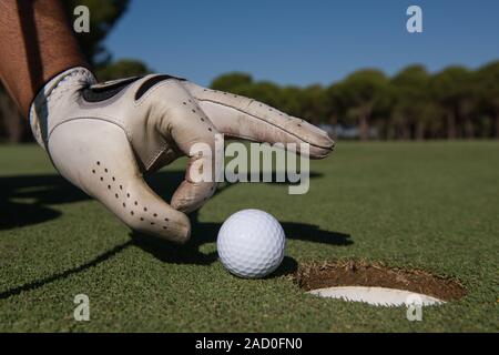 Des Menschen Hand Golf Ball im Loch Stockfoto