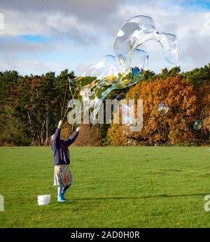 Eine Frau, die in einem öffentlichen Park in Bournemouth, Großbritannien, große Blasen bläst Stockfoto