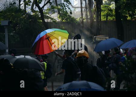 Hong Kong. Okt 2019 20. Eine schwarz gekleidete Demonstrant kann mit einem Regenbogen Regenschirm als behelfsmäßiger Schild vor einer Polizeistation gesehen werden. Stockfoto