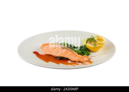 Gebackene Lachssteak mit Blattspinat und Zitronenscheibe isoliert auf weißem Hintergrund Stockfoto