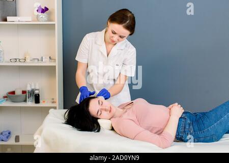 Schönheit haare, Mesotherapie: eine Kosmetikerin trichologist Arzt untersucht den Kopf einer jungen hübschen Frau in Spa Kosmetik center Stockfoto