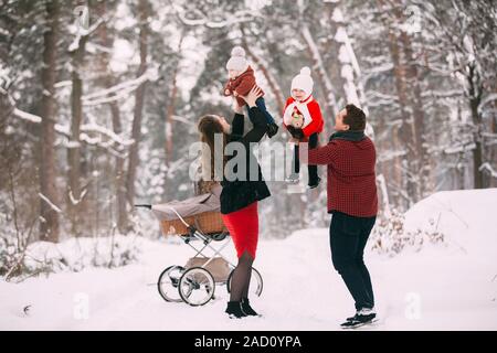 Eine schöne Familie mit retro Kinderwagen Spaziergänge durch den Winter schneebedeckten Wald. Mutter, Vater, Tochter und Sohn Tag im Freien genießen. Urlaub, Chris Stockfoto