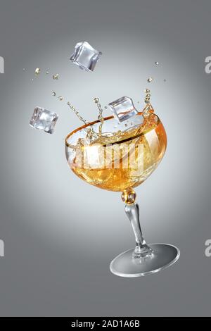 Frische Farbe orange Cocktail mit Eis im Weinglas auf grauem Hintergrund. Studio geschossen von Trinken im Freeze Motion, fliegende Eis, Tropfen in Spritzwasser. Clipp Stockfoto