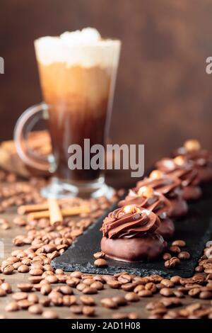 Dessert Schokolade mit Haselnuss und Irish Coffee mit Sahne auf einem Holztisch. Kaffeebohnen und Zimtstangen liegen auf dem Tisch verstreut. Stockfoto